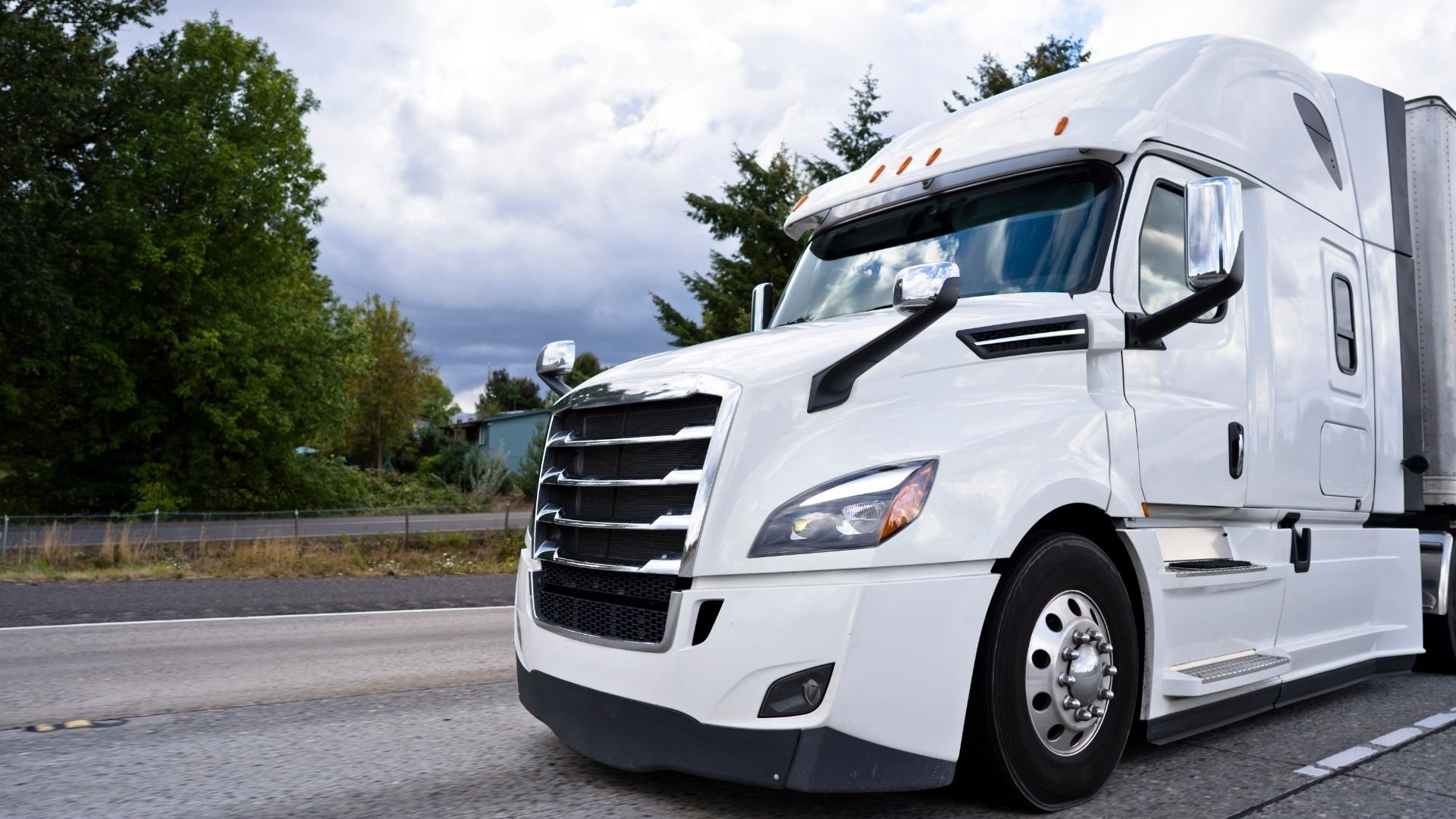 White semi truck cab parked on asphalt with trees in background under cloudy sky
