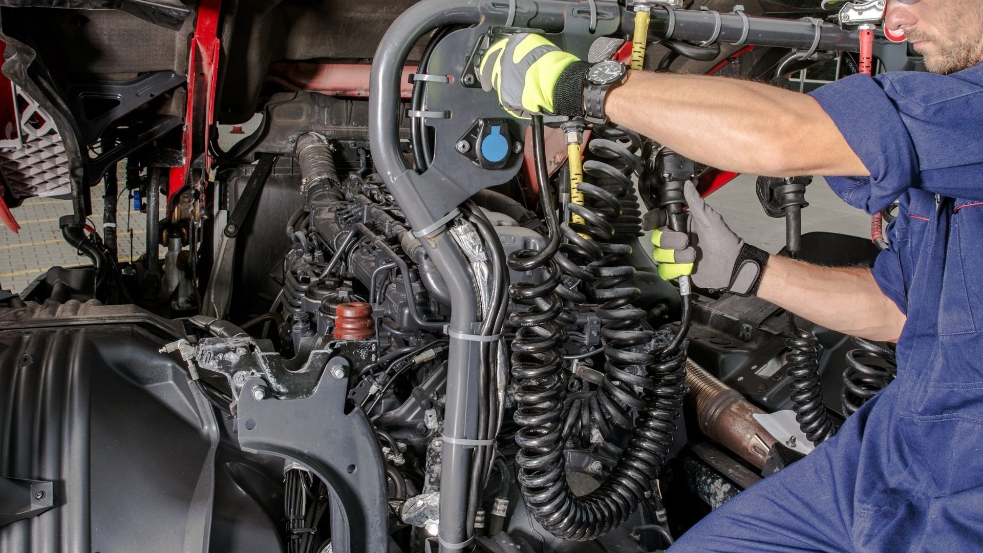 Mechanic in safety gear inspecting vehicle engine compartment with tools