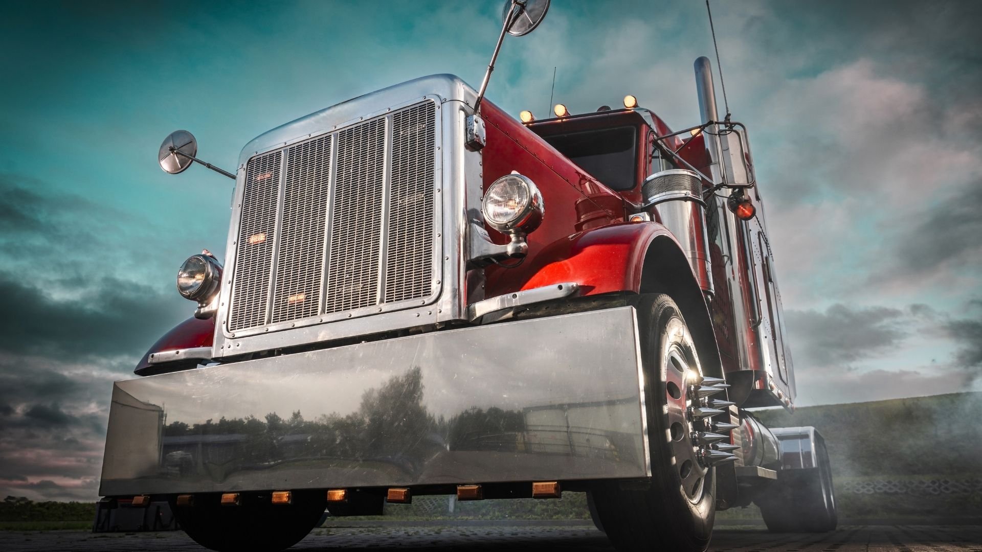 Red and silver vintage semi truck with large grille against dramatic turquoise sky