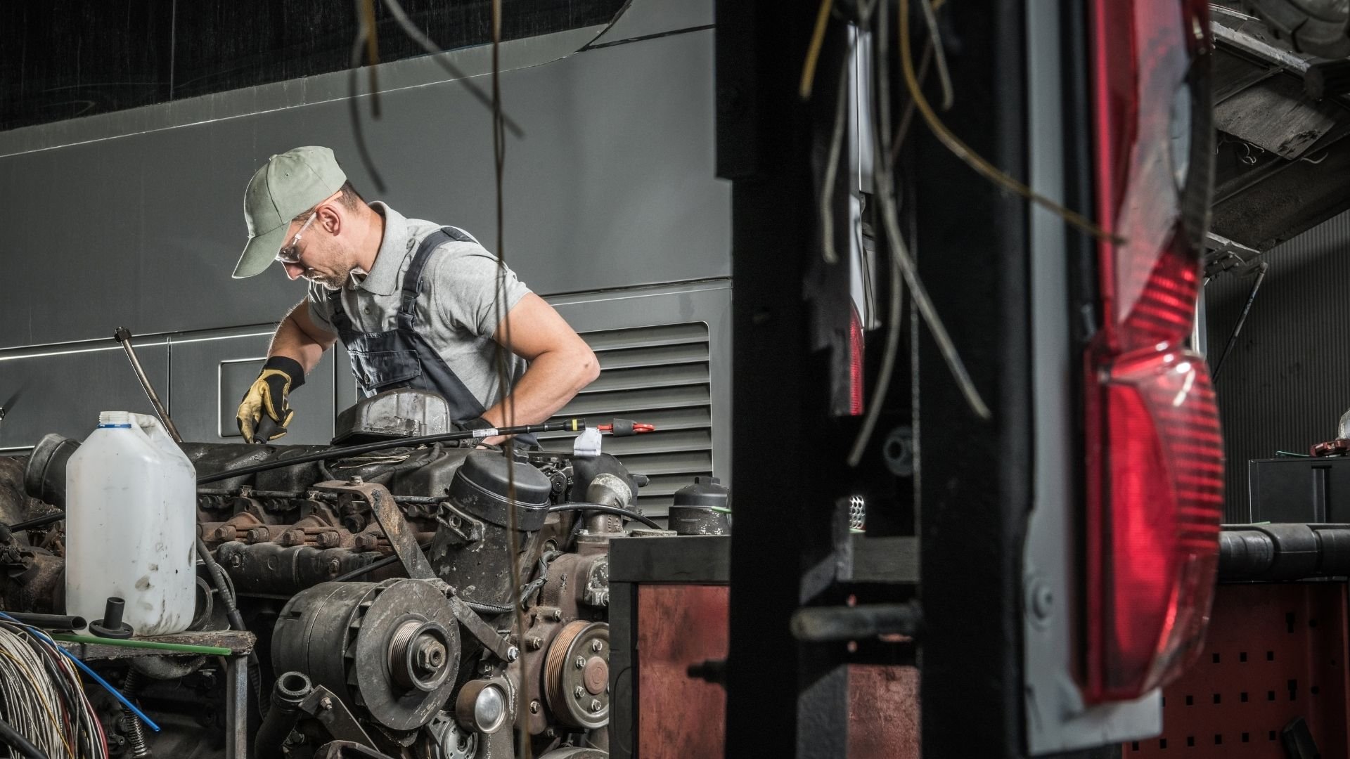 Mechanic in cap and gloves working on vehicle engine in repair shop