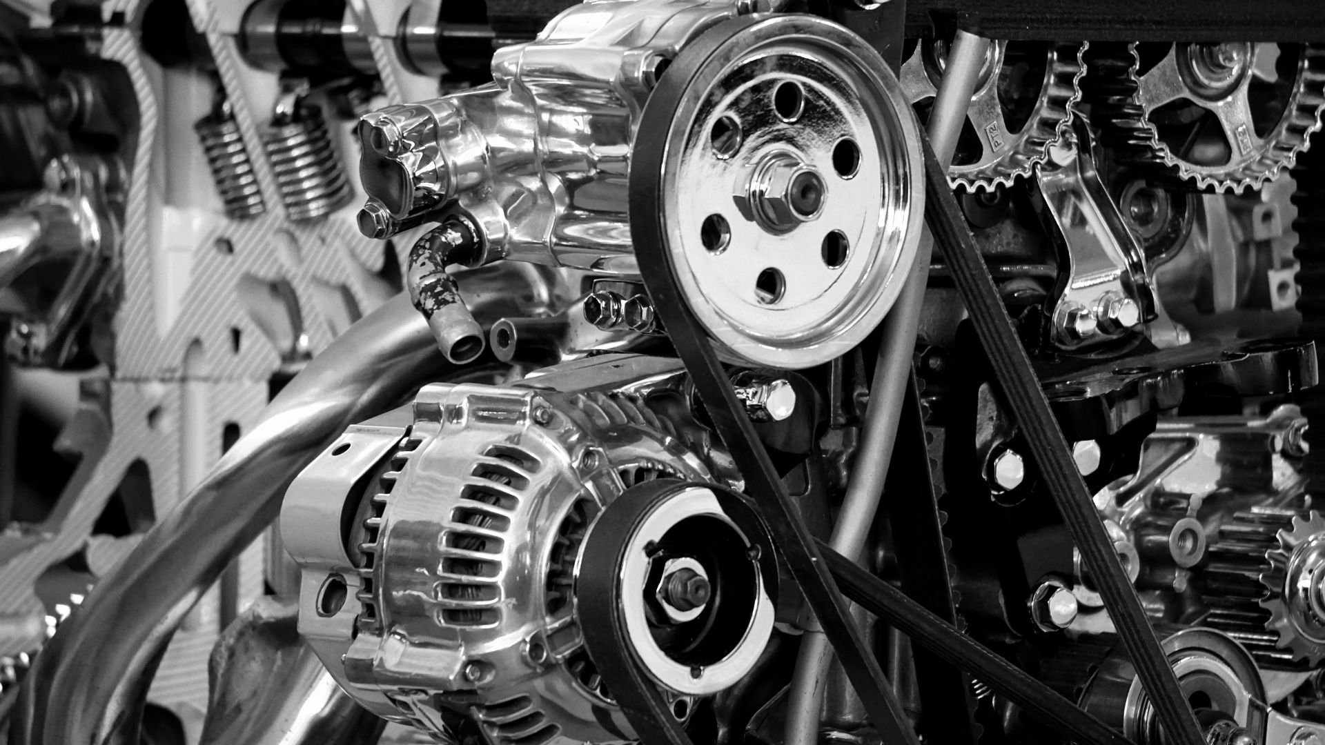 Close-up black and white image of shiny car engine components including pulley, alternator, and gears.