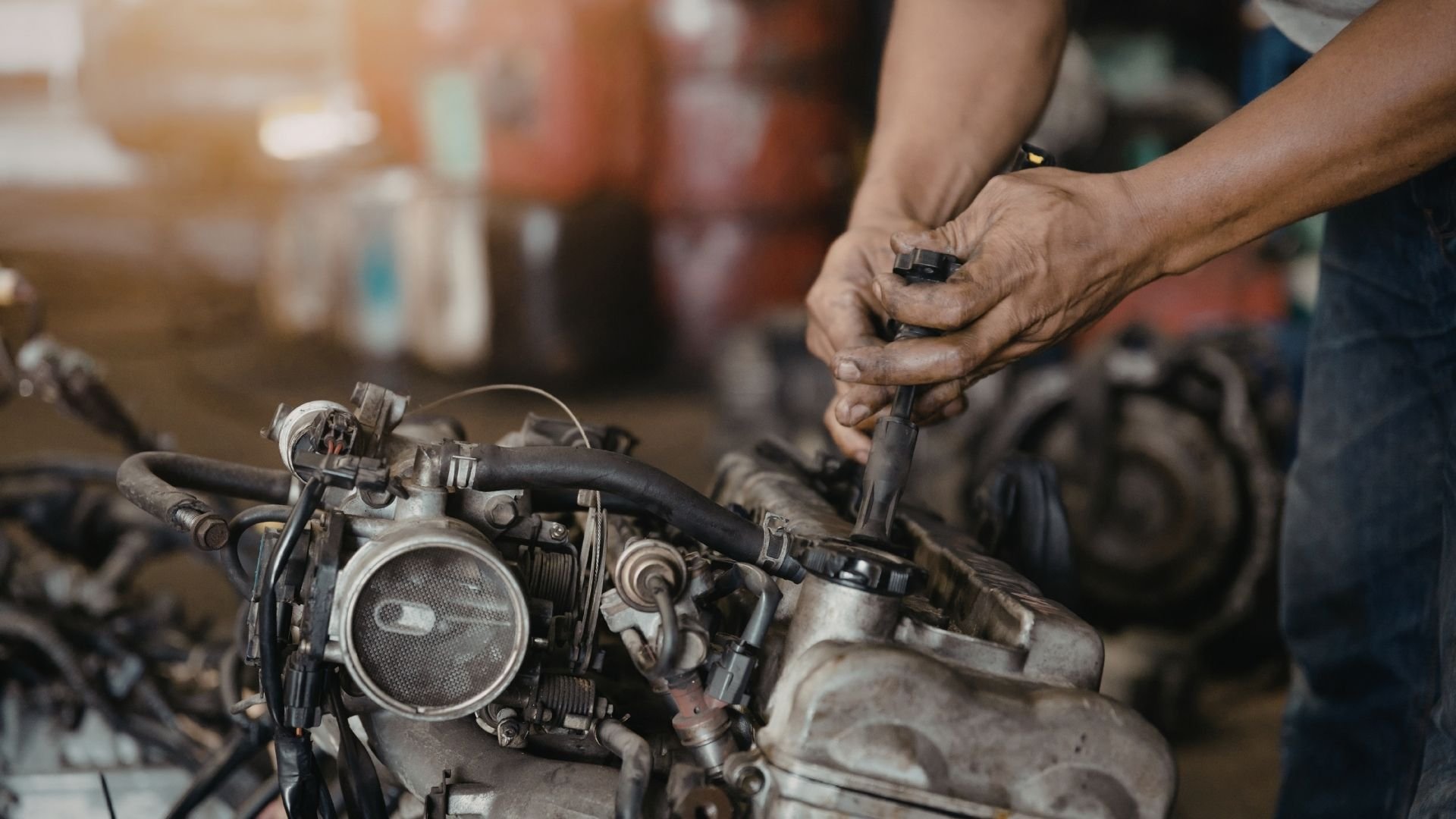 Mechanic's hands adjusting engine carburetor in workshop with tools visible.